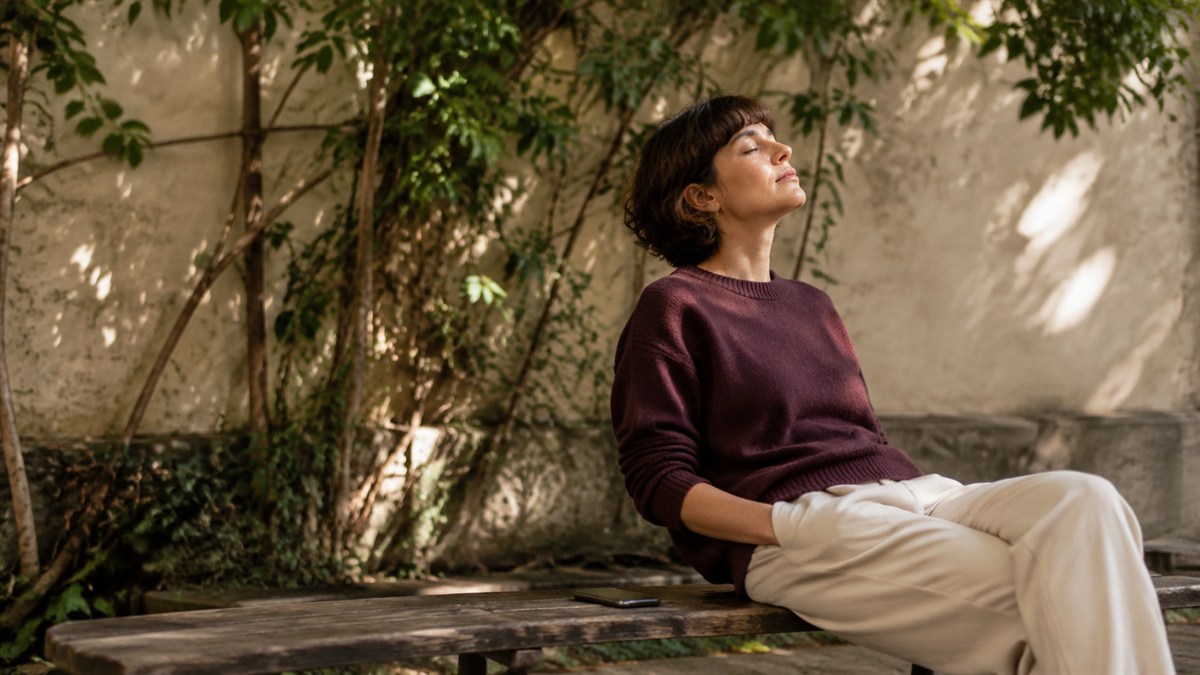 A woman rests with eyes closed on a bench, her phone set aside.